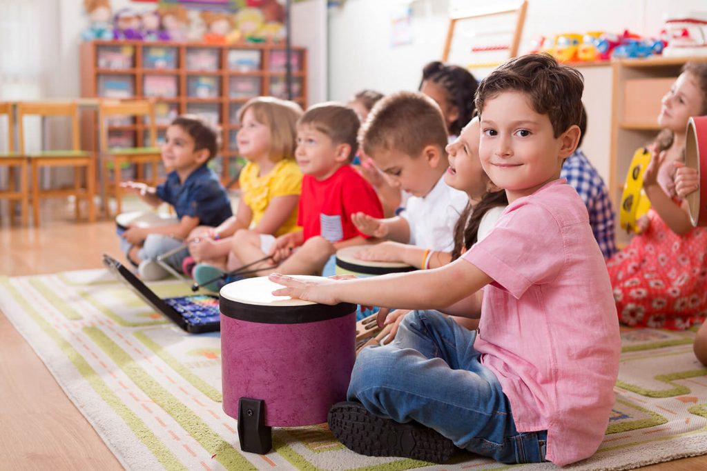 Young boy sitting on the floor patting a drum with other kids playing instruments at a childcare center in Parramatta, Blacktown Sydney