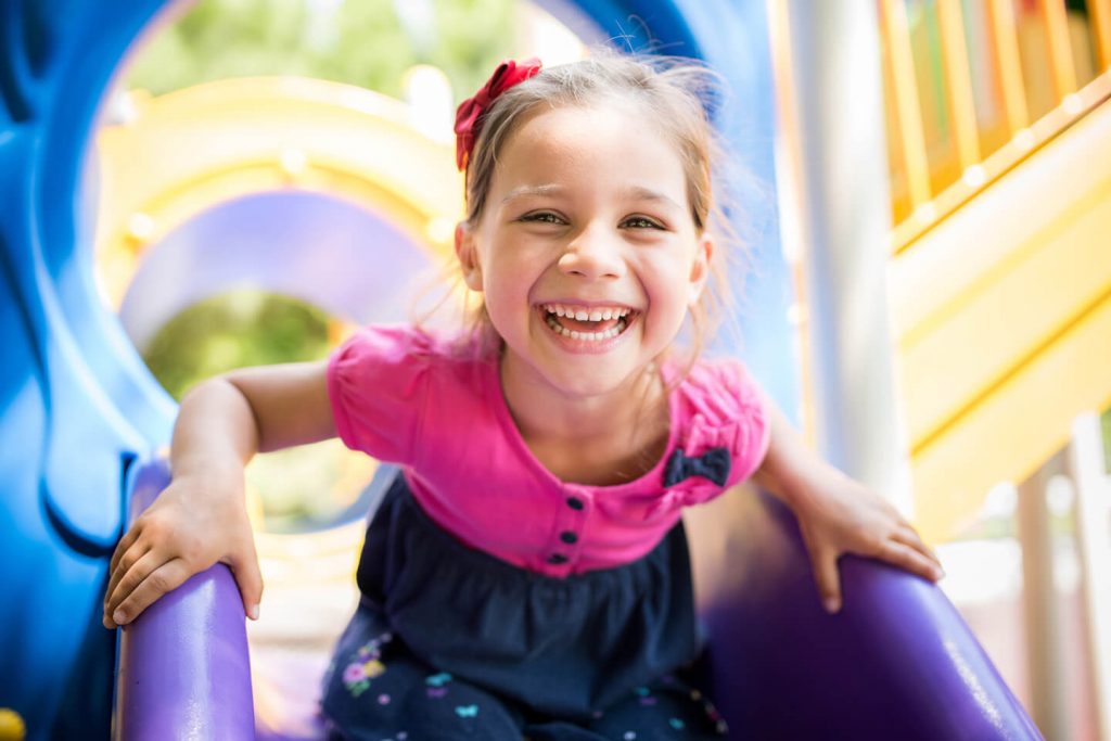 Young girl smiling while on a playground slide at a childcare center in the St George area of Sydney
