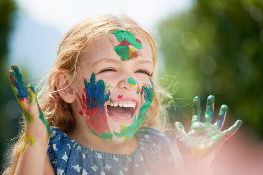 Young girl laughing while face painting on her face with her hands at a childcare center in Strathfield area Sydney